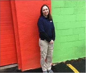 female, standing and posing in black servpro top by red and green wall