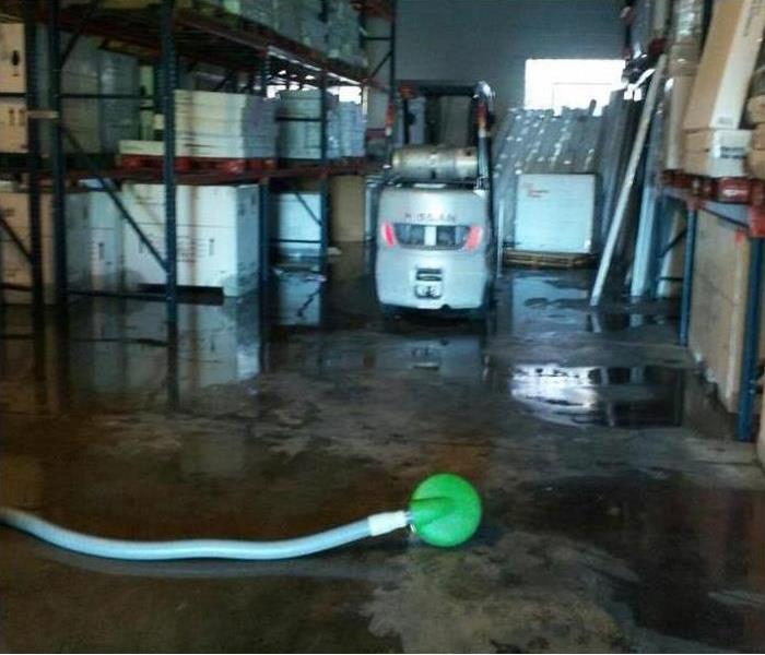 pump and blue hose on floor of wet warehouse, forklift there